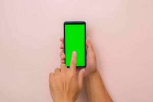 menselijk hand- gebruik makend van mobiel smartphone met mockup groen scherm Aan roze achtergrond. mannetje hand- tikken en snuifje naar zoom in of zoom uit Aan blanco digitaal scherm. foto
