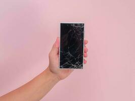 detailopname van hand- Holding mobiel telefoon met gebroken tintje scherm Aan roze achtergrond. vrouw hand- Holding oud telefoon met gebarsten en beschadigd scherm. foto