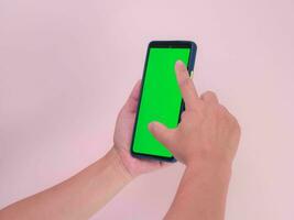 menselijk hand- gebruik makend van mobiel smartphone met groen scherm geïsoleerd Aan roze achtergrond. vrouw hand- aanraken en snuifje naar zoom in of zoom uit Aan digitaal blanco scherm Scherm en communicatie. foto