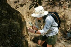 vrouwelijke geoloog die een vergrootglas gebruikt, onderzoekt de natuur en analyseert rotsen of kiezelstenen. onderzoekers verzamelen monsters van biologisch materiaal. milieu- en ecologisch onderzoek. foto