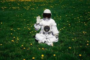 futuristische astronaut in een helm zit op een groen gazon tussen bloemen foto