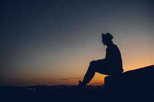 silhouet van een man die naar de zonsondergang over de stad kijkt foto