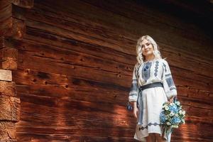 mooie vrouw in geborduurd shirt in de buurt van een houten huis foto