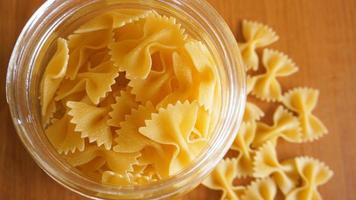 pasta in de vorm van bogen verspreid uit glazen pot.
