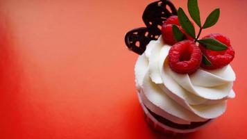 zoet dessert, cupcake met boterroom en framboos op rood