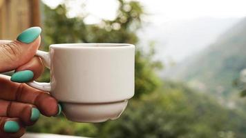 hand witte kop warme koffie. in de ochtend, koud uitzicht op de bergen foto