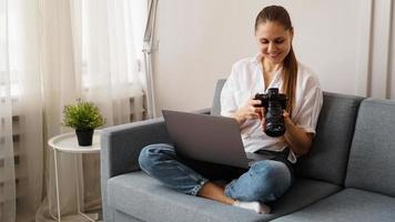 gelukkige jonge vrouw met fotocamera die laptop thuis gebruikt foto