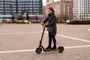 mooi meisje in een jas rijdt elektrische scooter door de stad