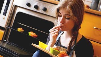 mooie blonde vrouw die muffins laat zien terwijl ze er een eet in een keuken foto