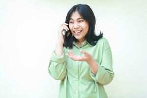 blij mooi Aziatisch vrouw lachend van grappig gesprek terwijl pratend Aan smartphone vervelend groen te groot overhemd staand over- geïsoleerd wit achtergrond foto