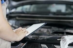 licentie technicus in garage gebruik makend van tablet naar volgen checklist terwijl aan het doen onderhoud Aan auto. dichtbij omhoog schot van deskundige in auto reparatie winkel aan het doen controle Aan voertuig radiator foto