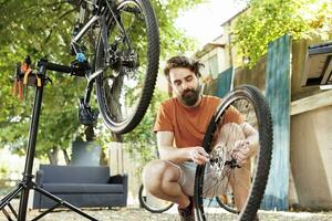 een toegewijd sportief Kaukasisch mannetje het uitvoeren van fiets onderhoud Aan zijn eigen buitenshuis zomer werkzaamheid. jong enthousiast Mens aan het doen jaar- onderhoud en repareren van modern fiets. foto
