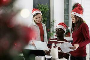 medewerkers werken samen Aan professioneel team project gedurende Kerstmis vakantie seizoen. multi-etnisch bedrijf team analyseren statistieken, gegevens grafieken en grafieken in feestelijk versierd kantoor foto