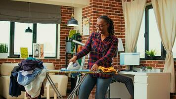 vrouw volwassen genieten van aan het doen wasserij werk Bij huis, hebben pret luisteren naar muziek- en strijken gewassen kleren. gelukkig huisvrouw dansen en het zingen terwijl ze doet klusjes, ijzer met stoom. foto