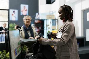 Afrikaanse Amerikaans werknemer scannen blouse streepjescode gebruik makend van op te slaan scanner, bespreken handelswaar korting met ouderen klant. senior klant buying modieus kleren in winkel winkel foto