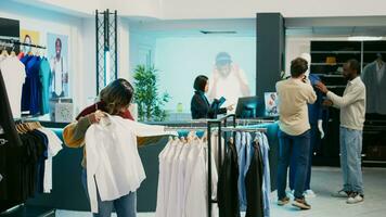 vrouw klant op zoek Bij handelswaar in kleding op te slaan, boodschappen doen voor nieuw modieus verzameling. jong vrouw controle kleren hangende in afdeling op te slaan, modern mode boetiek. foto