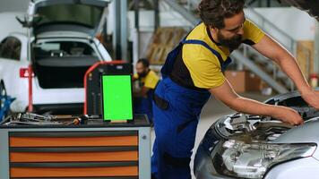 pannen schot van chroma sleutel tablet in garage werkruimte zittend Aan werk bank. mockup apparaat in auto onderhoud De volgende naar professioneel gereedschap met reparateurs in achtergrond opknappen beschadigd voertuigen foto