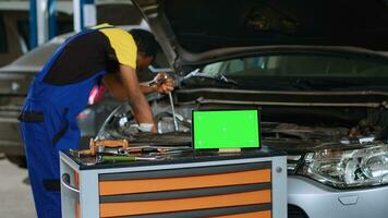 ingenieur in auto onderhoud toepassingen koppel moersleutel naar beveiligen bouten binnen voertuig met groen scherm tablet in voorkant. deskundige maakt gebruik van professioneel gereedschap naar herstellen uit van bestellen auto- De volgende naar mockup apparaat foto