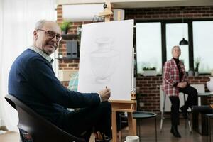 creatief hobby's voor volwassenen. glimlachen volwassen Mens zittend Bij kunst studio ruimte, ontwikkelen creativiteit in pensioen, aan het leren naar trek na 50 jaar. mensen uitdrukken zich door tekening foto