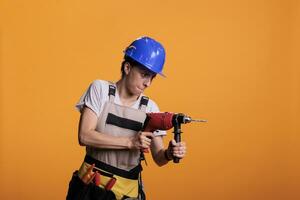 vrouw industrieel ingenieur Holding boren geweer in nieuw interieur vernieuwing projecteren, gebruik makend van macht boren nagel pistool. vrouw renovator vervelend uniform in studio schot over- geel achtergrond. foto