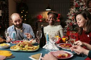 Afrikaanse Amerikaans vrouw Bij Kerstmis avondeten vieren winter vakantie met mensen bijeenkomst Bij tafel en aan het eten traditioneel eigengemaakt maaltijd. groep van vrolijk personen genieten van Kerstmis evenement Bij huis. foto