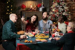 personen genieten van foto's Aan Kerstmis vooravond feest, vieren december vakantie samen in de omgeving van de tafel. maken selfies en afbeeldingen gedurende avondeten evenement, hebben pret met smartphone. foto