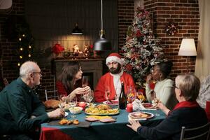 persoon de kerstman claus cosplay Bij avondeten maken mensen lach en vieren Kerstmis vooravond feest samen. senior mensen, vrienden en familie bijeenkomst in de omgeving van tafel naar eten en drinken Aan vakantie. foto