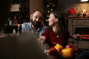 zoet mensen vergadering familie Bij avondeten Aan Kerstmis vooravond, bijeenkomst in de omgeving van tafel met vrienden en familieleden naar eten traditioneel voedsel en drinken wijn. paar pratend naar personen gedurende december evenement. foto