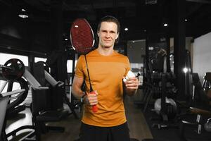 slim professioneel badminton speler met racket en veer shuttle staand portret in Sportschool sport club spier geschiktheid opleiding foto