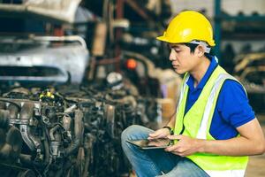 ingenieur mannetje arbeider controleren voorraad op te slaan oud gebruikt auto Reserve een deel motor uitrusting een deel lijst voor uitverkoop recycle in reparatie auto garage markt foto