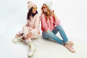 twee vrienden chillen Aan wit verdieping in studio. schattig roze kleding. elegant schoenen. foto