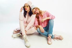 twee moe vrienden chillen Aan wit verdieping in studio. schattig roze kleding. elegant schoenen. foto