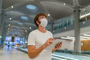 Mens in gasmasker masker is aan het wachten De volgende vlak Bij de luchthaven en gebruik makend van tablet. coronavirus covid-19 concept. foto