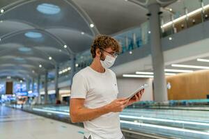 Mens in gasmasker masker is aan het wachten De volgende vlak Bij de luchthaven en gebruik makend van tablet. coronavirus covid-19 concept. foto