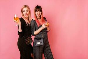 elegant vieren Dames in partij jurk drinken shampagne en hebben Super goed tijd samen. roze achtergrond. gelukkig emoties. modieus kleding. foto