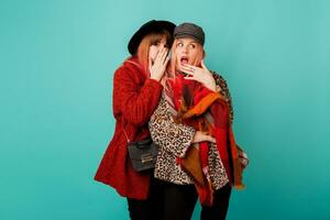 twee elegant blond Dames poseren in studio Aan blauw turkoois achtergrond. vrienden roddelen en hebben pret samen. vervelend luipaard afdrukken faux vacht jas en wol sjaal. winter mode. foto