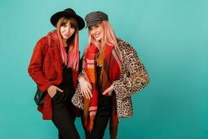 modieus studio schot van twee elegant modellen in helder winter of herfst kleding, hoed en sjaal poseren in turkoois achtergrond. foto