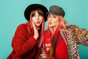 dichtbij omhoog studio portret van twee mooi schattig modellen met roze haren in elegant luipaard afdrukken faux vacht jas en modieus hoed Aan turkoois. verrassing gezicht. winter modieus kleding. foto
