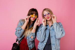 levensstijl portret van twee hipster meisjes het beste vrienden met helder maken omhoog , maken grappig gezichten en Bezig met verzenden kus over- roze achtergrond. foto