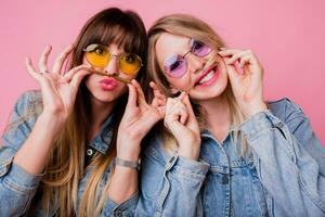 levensstijl portret van twee hipster meisjes het beste vrienden met helder maken omhoog , maken grappig gezichten en Bezig met verzenden kus over- roze achtergrond. foto