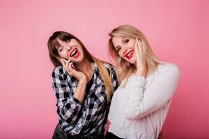 brunette vrouw met verrassing gezicht pratend door mobiel telefoon. haar het beste vriend lachend en hebben plezier. roze achtergrond. studio schot. foto