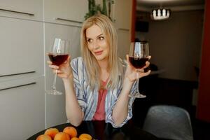 blond vrouw tasjes twee bril van rood wijn Aan haar eigen keuken. foto