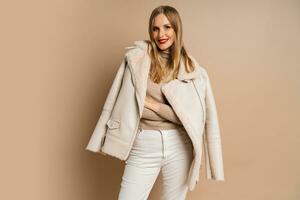 mooi legant blond vrouw met rood lippen vervelend modieus eco leer jasje , poseren over- beige achtergrond. winter mode trends. foto