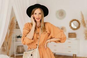 mooi blond vrouw in beige linnen jurk poseren in elegant boho interieur. foto