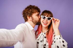 mooi vrouw met openhartig glimlach en roze haren poseren met haar vriendje met baard. hipster paar in liefde Aan Purper achtergrond. wijnoogst zonnebril. foto