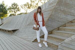 gelukkig elegant vrouw leerling poseren in modern park , ring wit jeans, jasje en t-shirt. vol lengte. foto