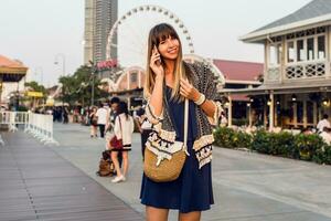 zomer positief portret van vrolijk vrouw in elegant kleding pratend door mobiel telefoon en glimlachen Aan rivierfront in Bangkok , ferris wiel en cafés achtergrond. foto