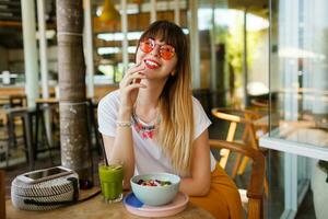 gelukkig elegant vrouw aan het eten gezond voedsel zittend in de mooi interieur met groen bloemen Aan de achtergrond. gezond voedsel concept. foto