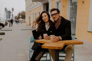 modieus paar in liefde zittend in straat cafe en drinken heet koffie terwijl op reis in Europa. foto