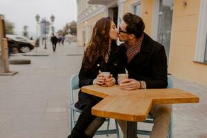 modieus paar in liefde zittend in straat cafe en drinken heet koffie terwijl op reis in Europa. foto